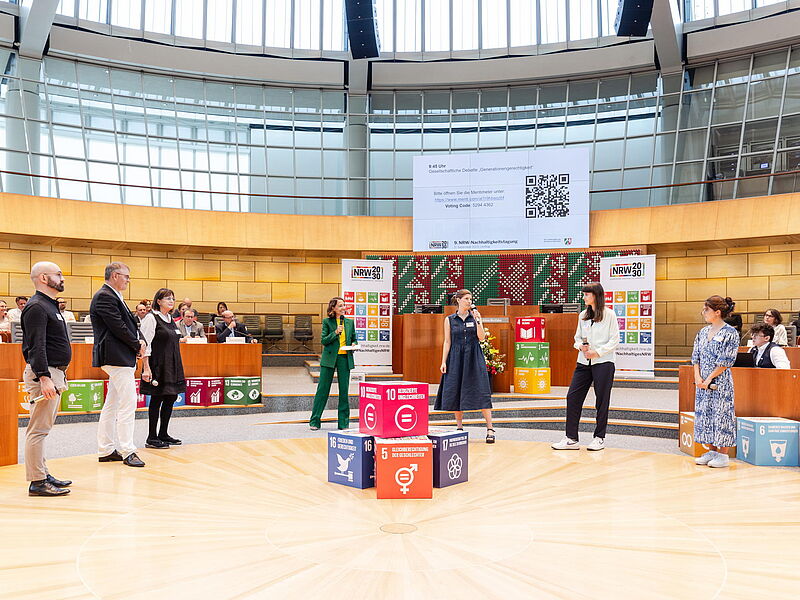 Das Bild zeigt unsere Schülerin im Landtag in NRW vor den Würfeln mit den SDGs